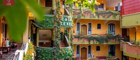 A multi-story building with balconies covered in greenery, a sign reading "CASA TEXEL," and a visible entrance.
