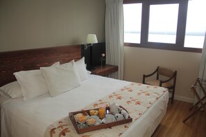 A hotel room with a bed, a bedside table with a lamp, a chair, and a window with a view. - Quirinale Hotel (Colon)