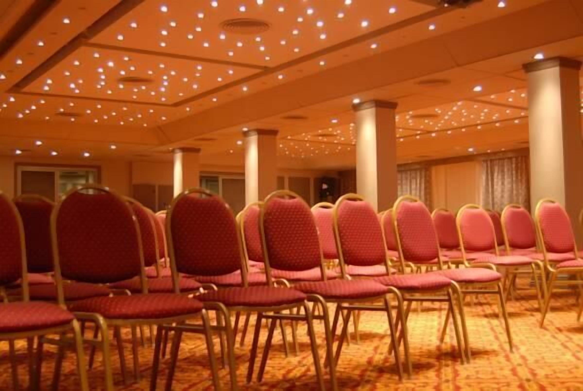 A conference room with rows of red chairs and a carpeted floor.