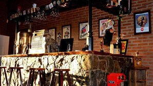A bar area with a stone counter, stools, a red coffee machine, and various framed advertisements on the wall. - Hosteria Lauquen Pilmaiquen y Spa (Merlo)