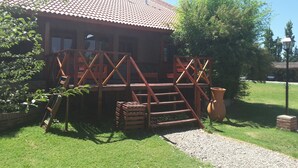 A wooden cabin with a tiled roof, a porch with wooden railings, and a gravel path leading to the entrance. - Hosteria Lauquen Pilmaiquen y Spa (Merlo)