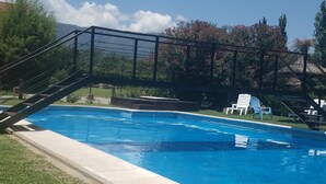 A swimming pool with a clear blue sky, a grassy area, and a wooden deck with chairs. - Hosteria Lauquen Pilmaiquen y Spa (Merlo)