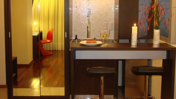Une cuisine compacte avec un plancher en bois, une chaise rouge, une petite table à manger avec une bougie et un vase rempli de fleurs.