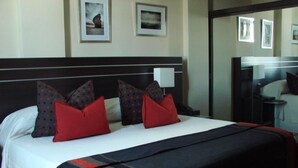 Une chambre d’hôtel avec un grand lit, deux tables de chevet, un miroir et des tableaux encadrés au mur.