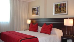 Une chambre d’hôtel avec un grand lit, des oreillers rouges, deux lampes de chevet et deux tableaux encadrés au mur.