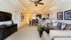 A living room with a flat-screen TV, a ceiling fan, a sofa, a coffee table, and a dining area with chairs and a table. - RVH 121 Centre Court Dream (Kissimmee)