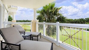 A balcony with a white railing, a chair, a table, and a view of a well-maintained lawn and palm trees. - RVH 121 Centre Court Dream (Kissimmee)