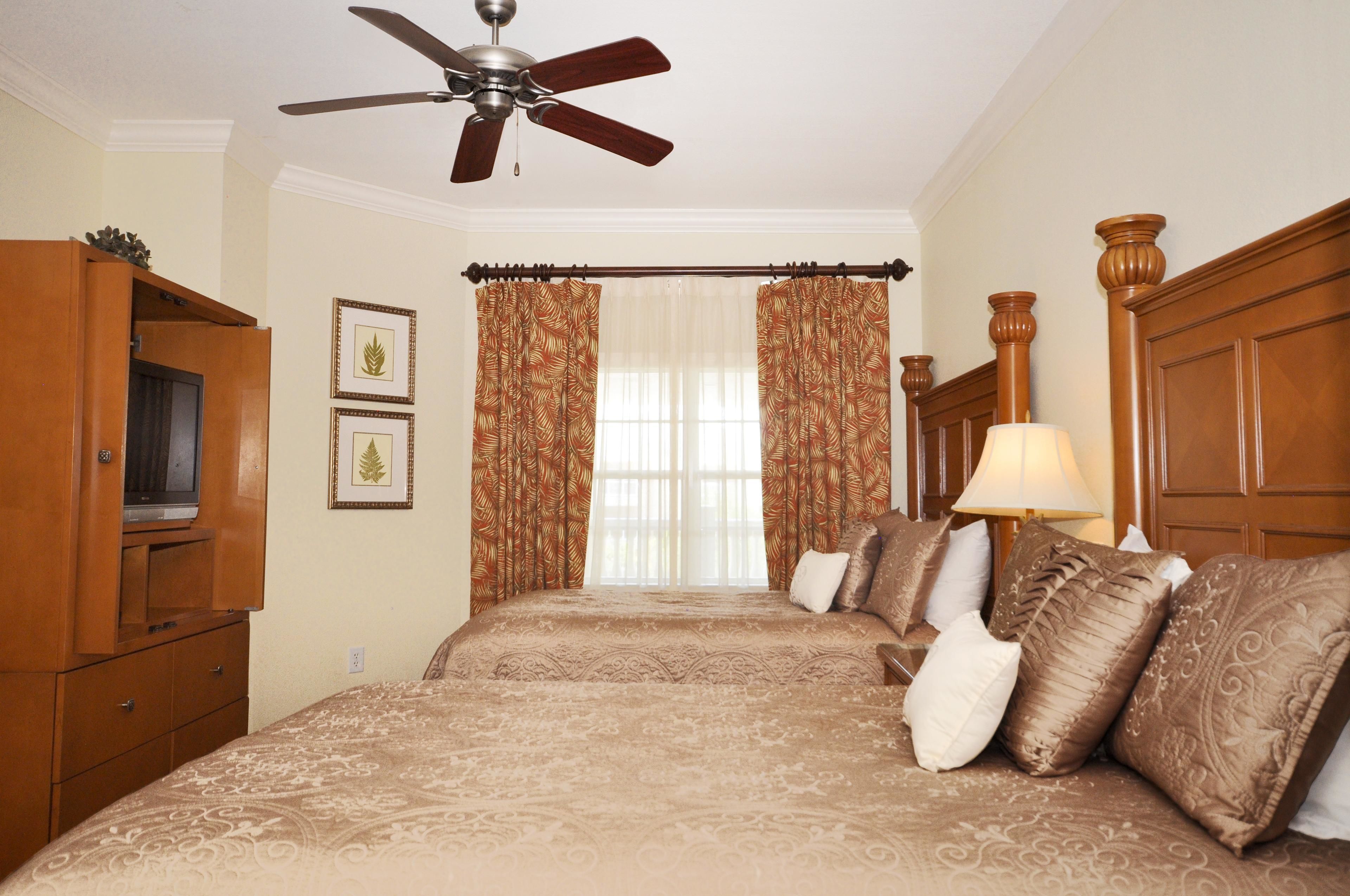 A bedroom with a bed, a ceiling fan, a television, and curtains.