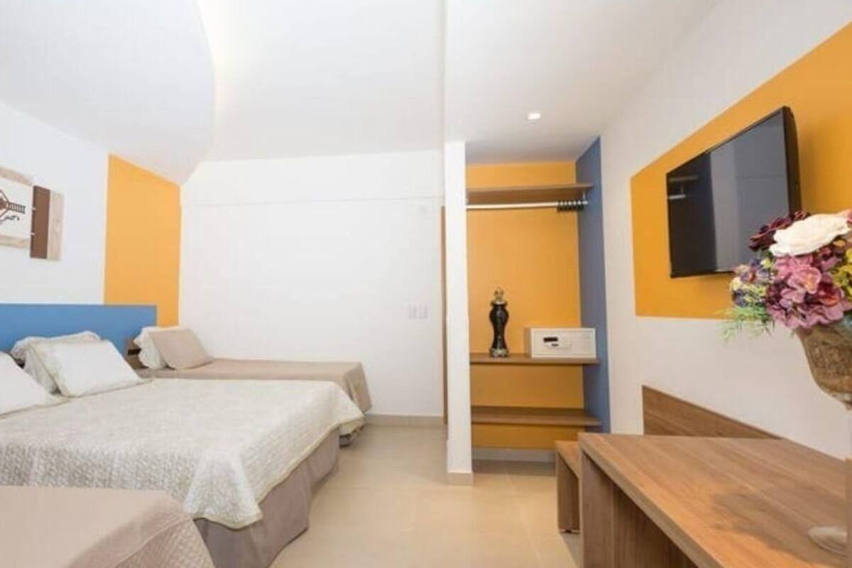 Een hotelkamer met twee bedden, een houten bankje, een televisie en een bloemenvaas.