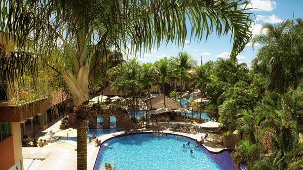 A pool area with palm trees, lounge chairs, and a clear blue pool. - Prive Thermas Hotel by WAM Experience (Caldas Novas)