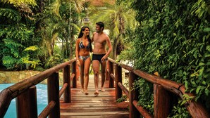 A wooden bridge with railings leading to a pool surrounded by lush greenery. - Prive Thermas Hotel by WAM Experience (Caldas Novas)