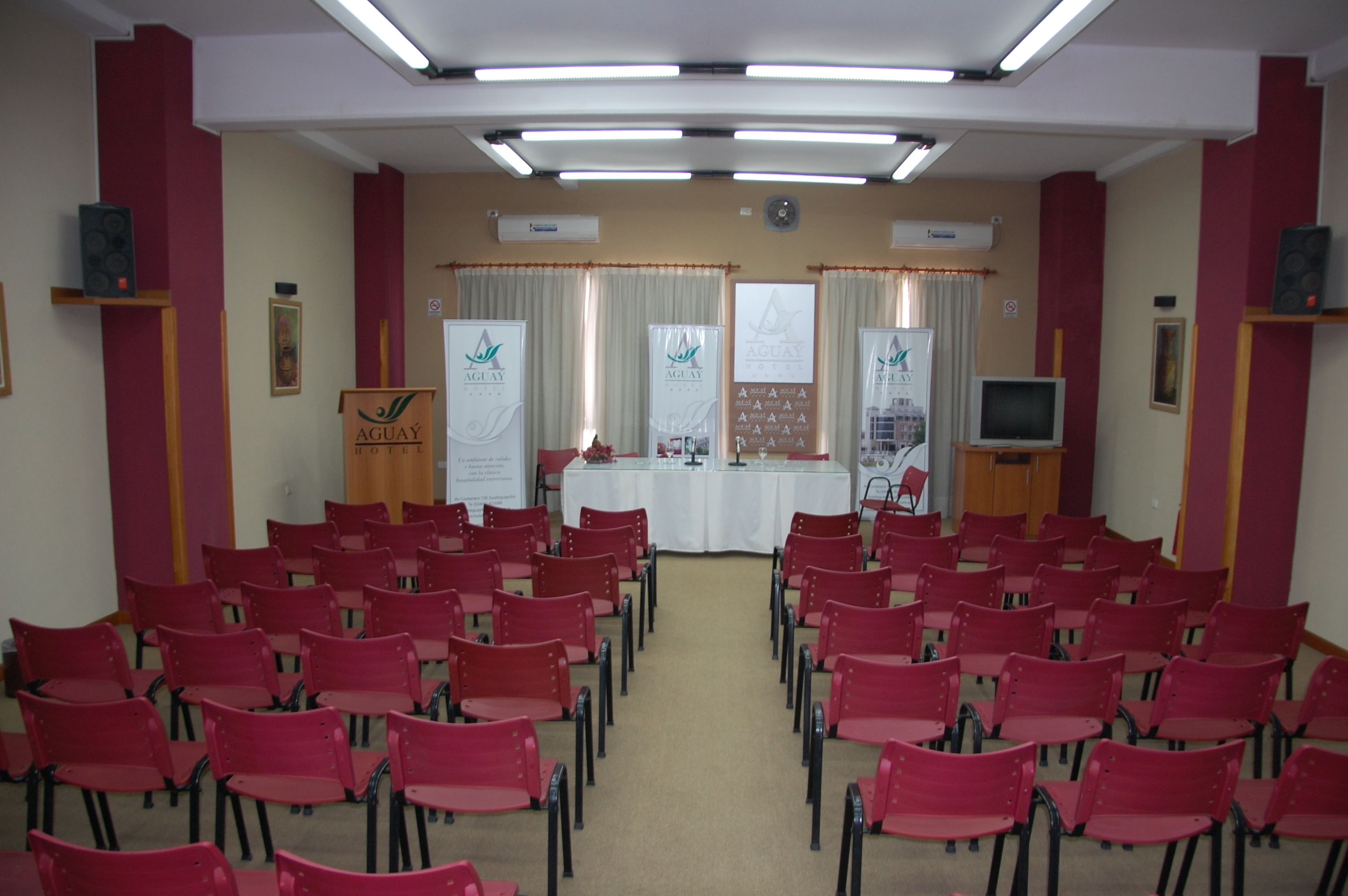 Una sala conferenze con file di sedie rosse, un podio e striscioni appesi alle pareti.