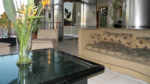Een moderne woonkamer met een glazen salontafel, een beige bank en potplanten.