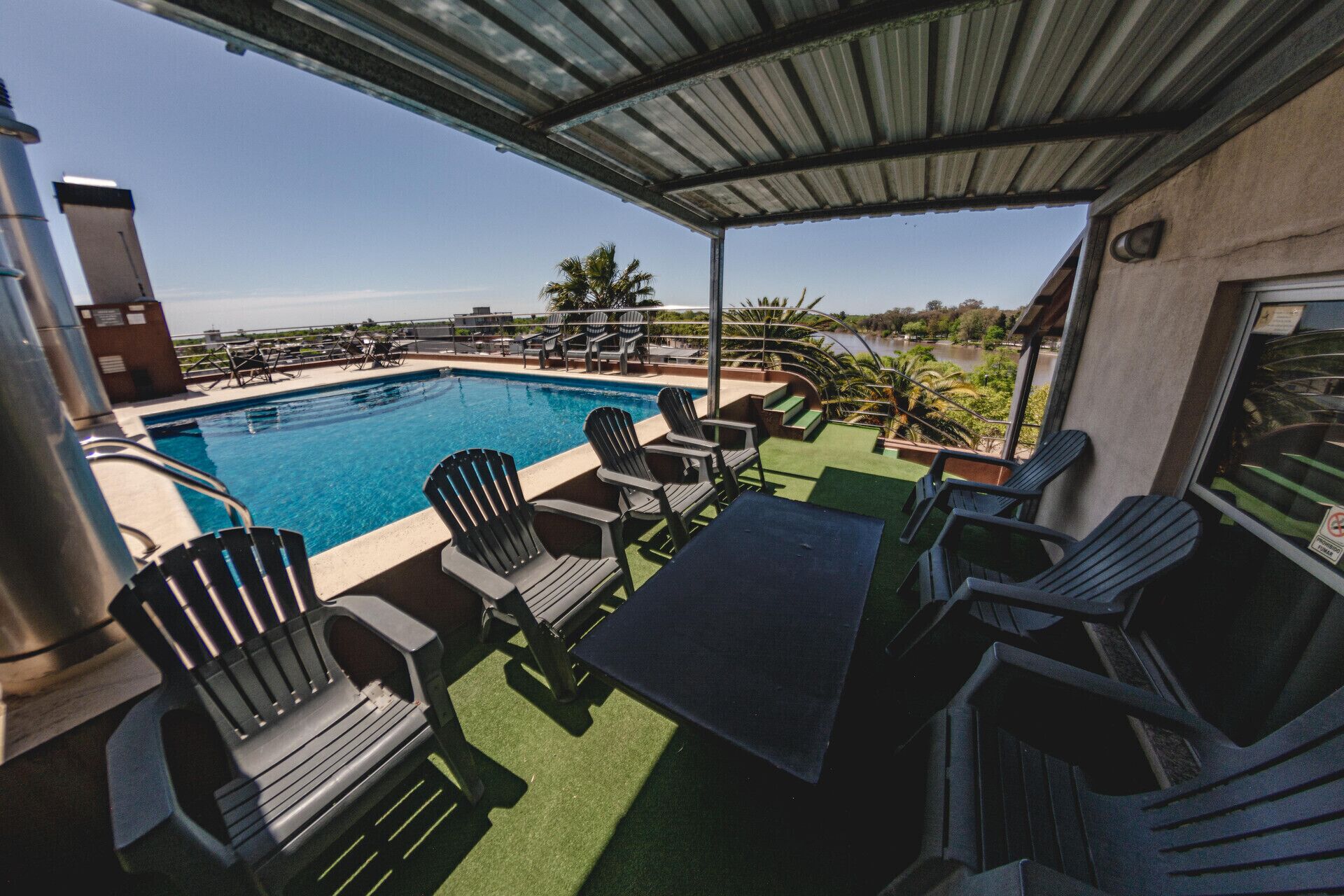A rooftop pool area with chairs and a table, surrounded by a covered patio.