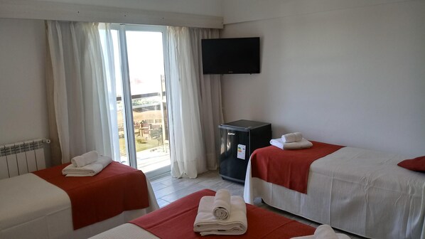 A hotel room with two beds, a television, a minibar, and a view of the outside.