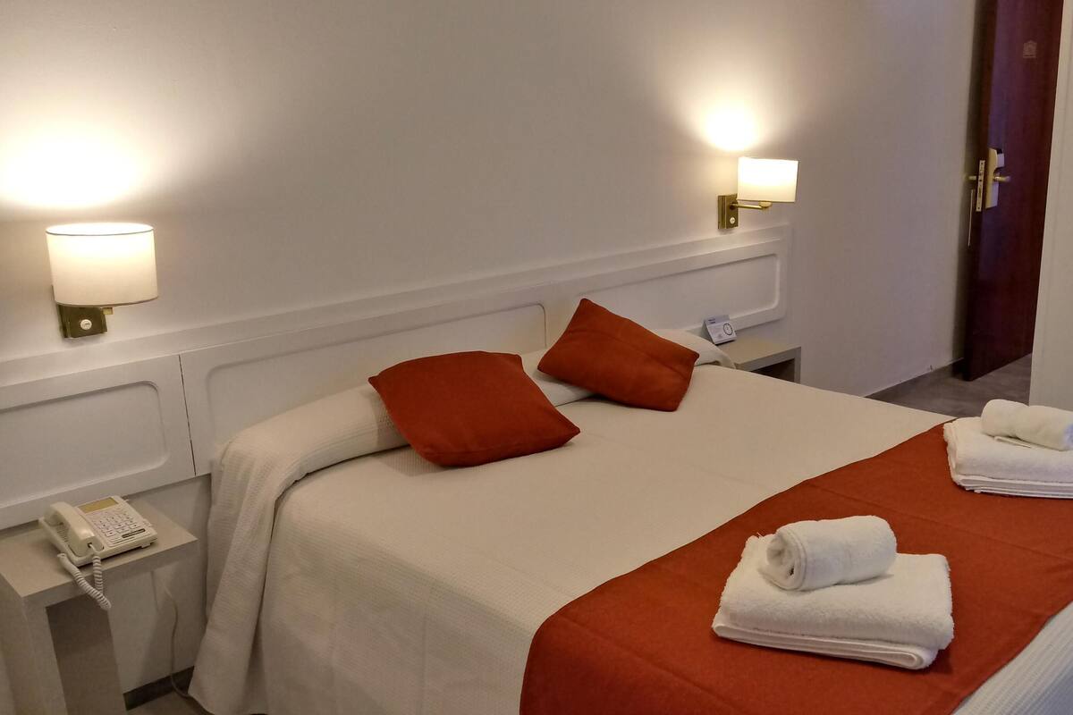 Ein Hotelzimmer mit einem Bett, zwei Kissen, einem Nachttisch mit Telefon und einer Wandlampe.