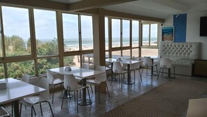 Een eetgedeelte met grote ramen met uitzicht op een strand, witte tafels en stoelen, en een gestuikt hoofdeinde.