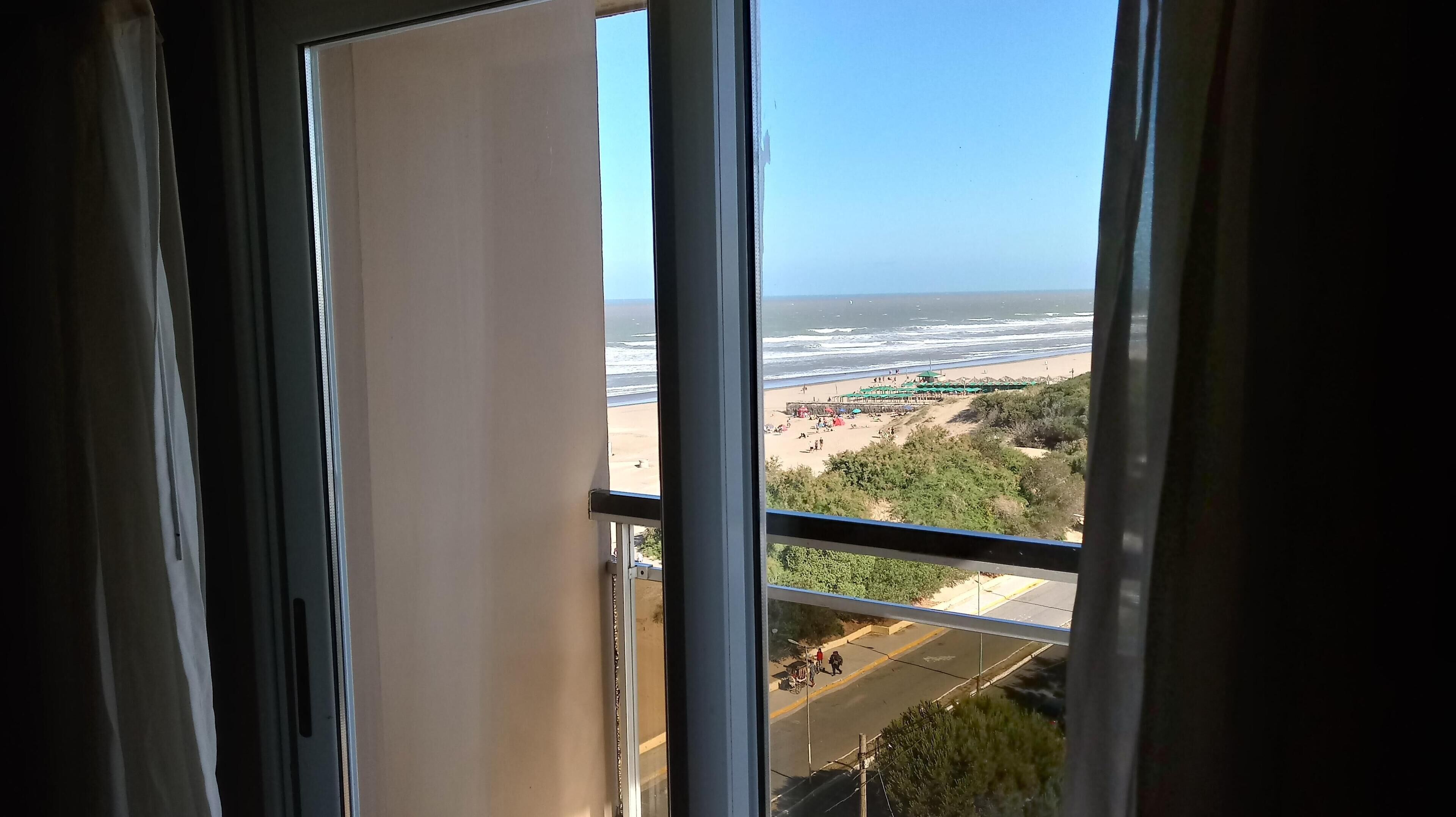Vista desde una ventana sobre una playa con sombrillas y gente.