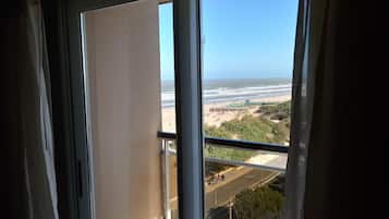 Vista desde una ventana sobre una playa con sombrillas y gente.
