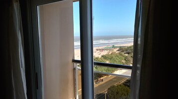 Vista desde una ventana sobre una playa con sombrillas y gente.