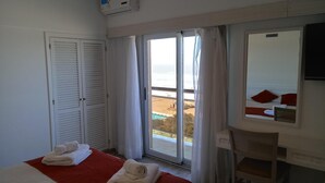 Een hotelkamer met een bed, een stoel, een raam met uitzicht op het strand en een deur met verstelbare luiken.