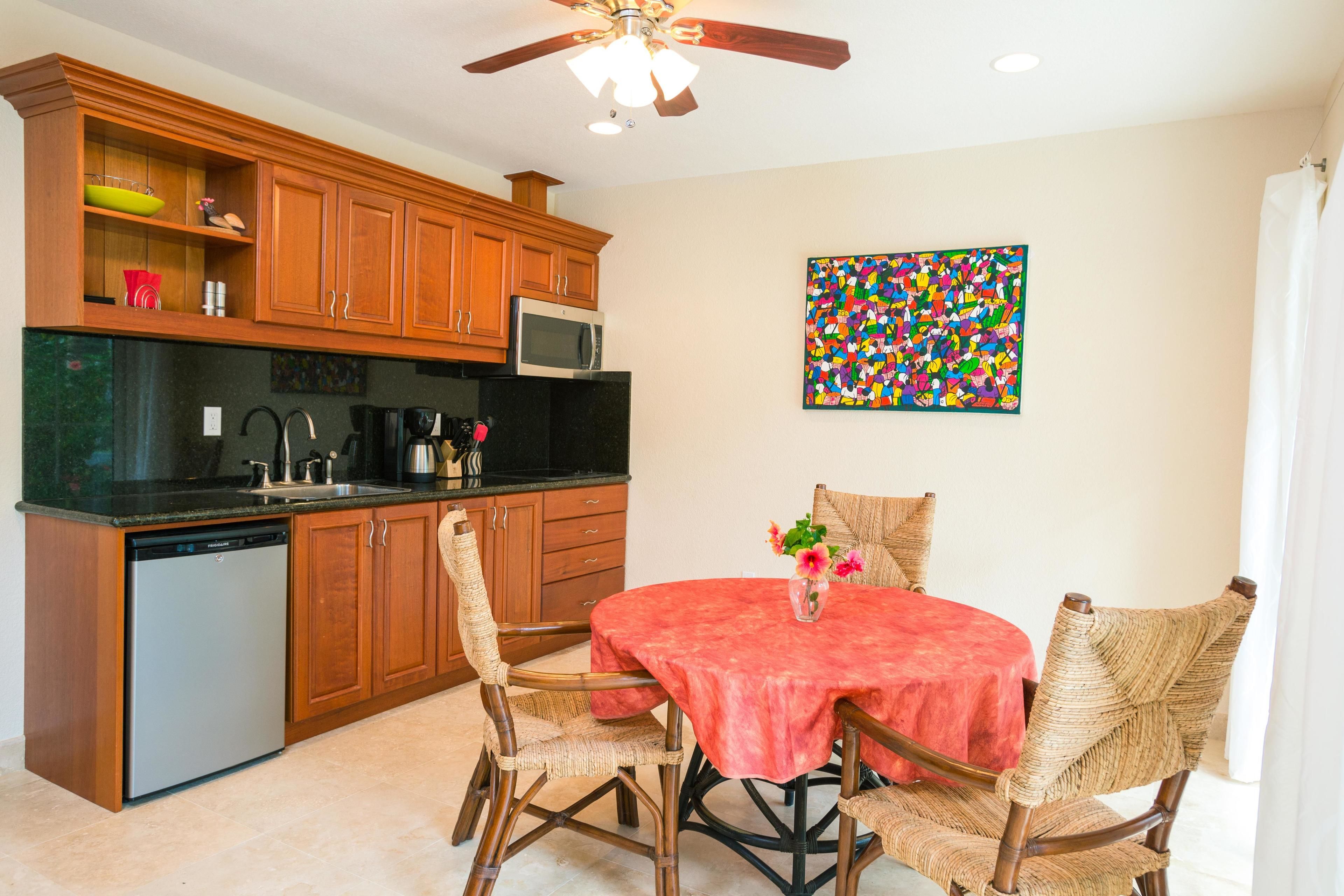 A kitchen with wooden cabinets, a microwave, and a dishwasher. There is a dining table with a red tablecloth and wicker chairs.