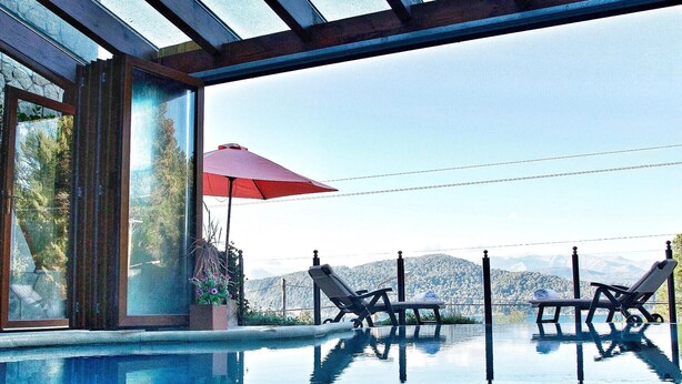 An infinity pool with two lounge chairs and a red umbrella, overlooking a mountainous landscape. - Bungalows Buena Vista (San Carlos de Bariloche)