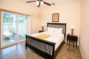 A bedroom with a bed, two bedside tables, a ceiling fan, and a sliding glass door leading to a balcony.