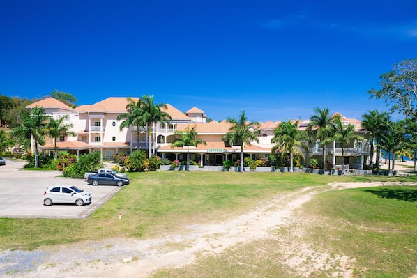 A hotel with multiple buildings, a parking area, and a grassy lawn with palm trees.