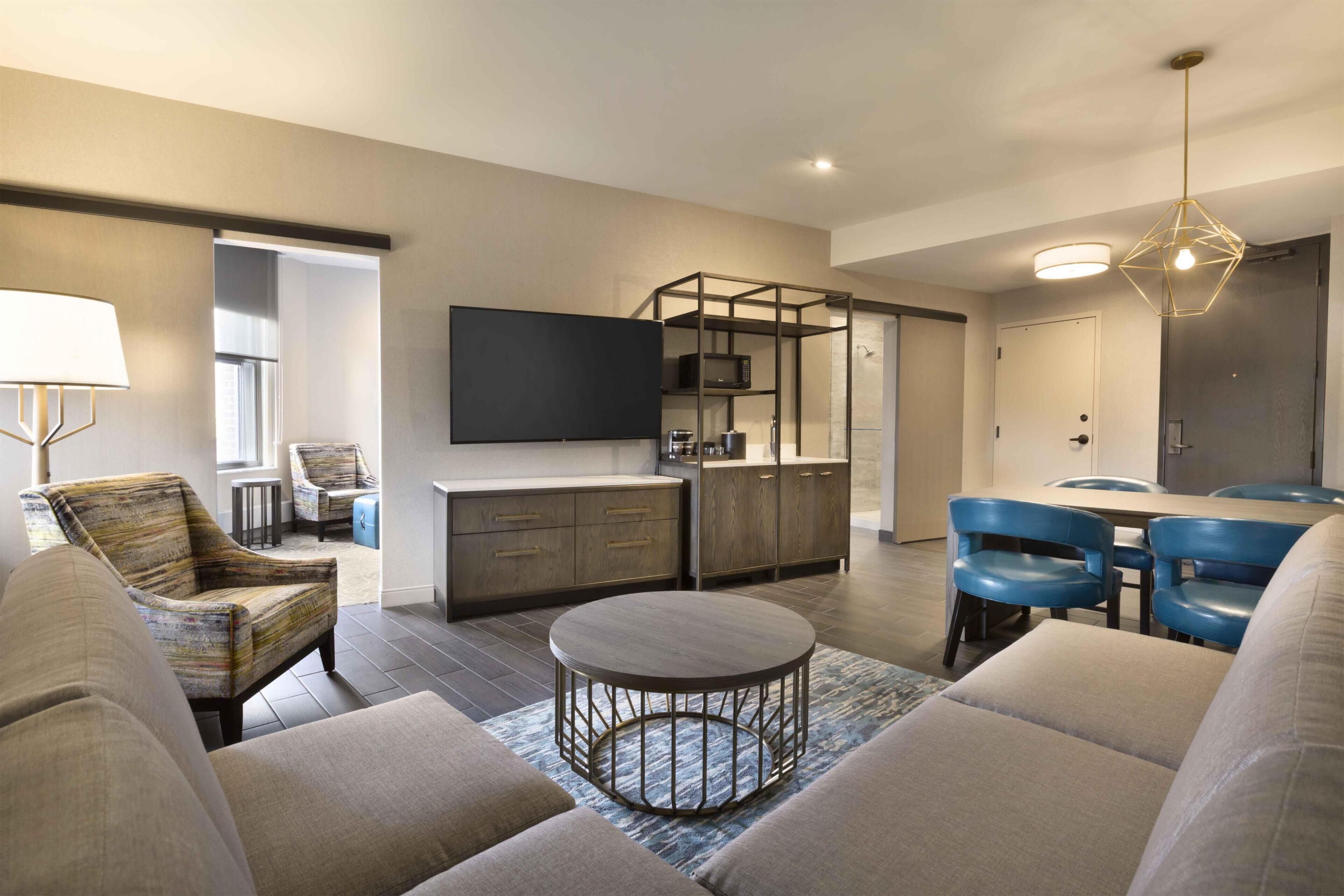 A modern living room with a sofa, a coffee table, and a dining area with blue chairs.