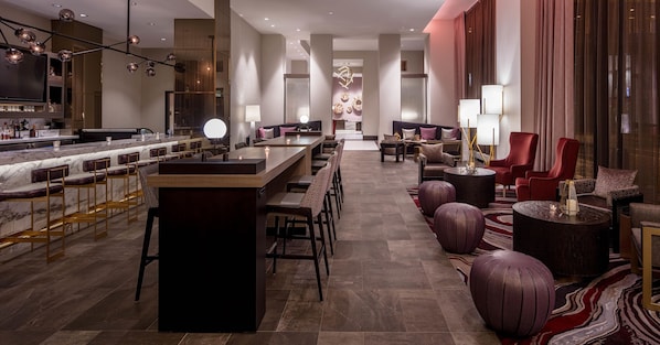 A modern hotel lobby with a bar area, seating, and a decorative wall.