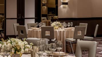 A formal dining area with tables set for multiple guests, featuring chairs, plates, cutlery, and glassware.