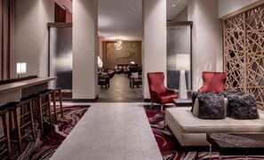 Un vestíbulo de hotel con piso de mármol, sillas rojas, un sofá y una pared decorativa.