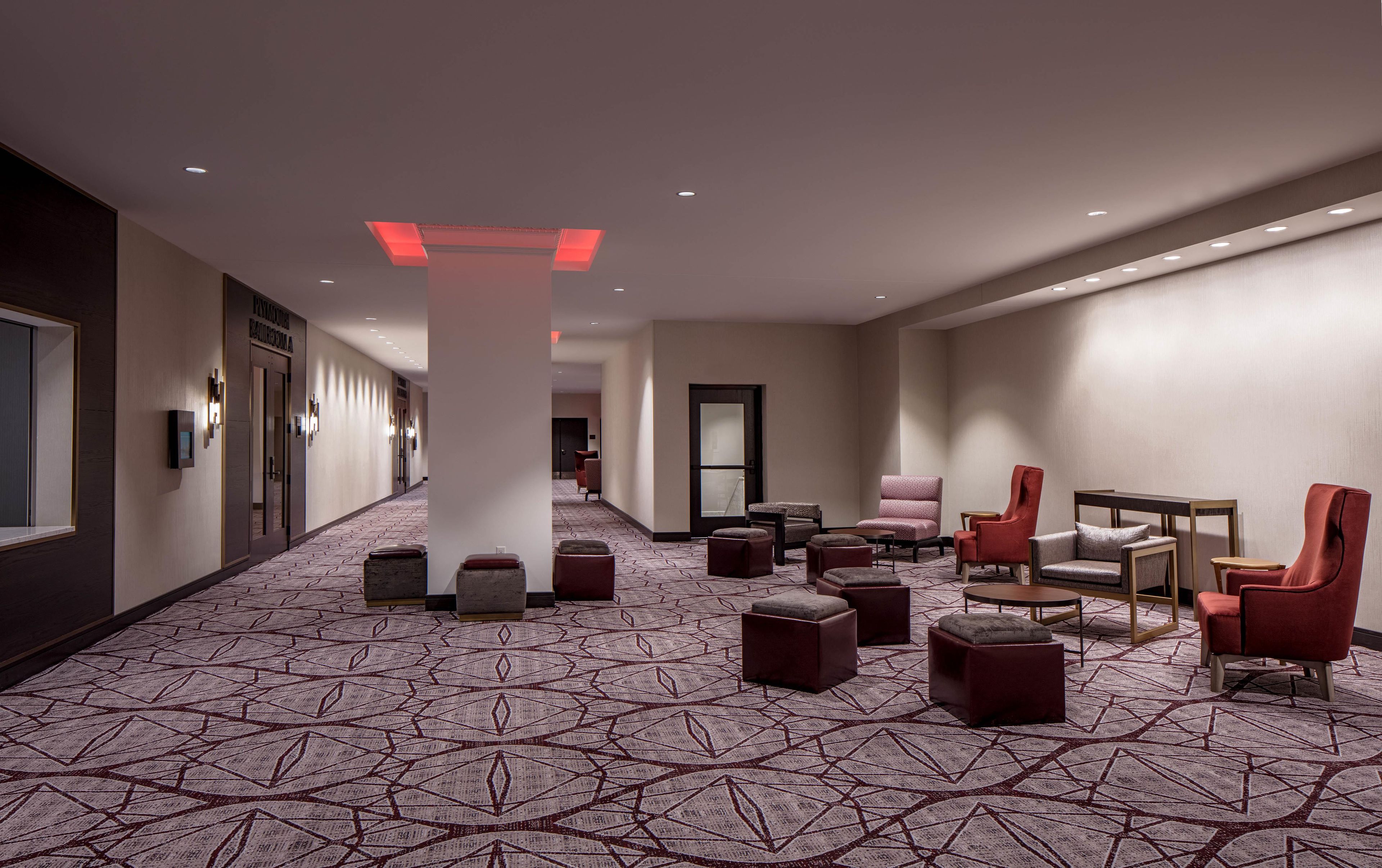 A hotel lobby with a patterned carpet, seating area with chairs and ottomans, and a reception desk.