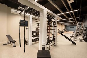 Un gimnasio con equipo de ejercicio, una banca y un televisor instalado en la pared.