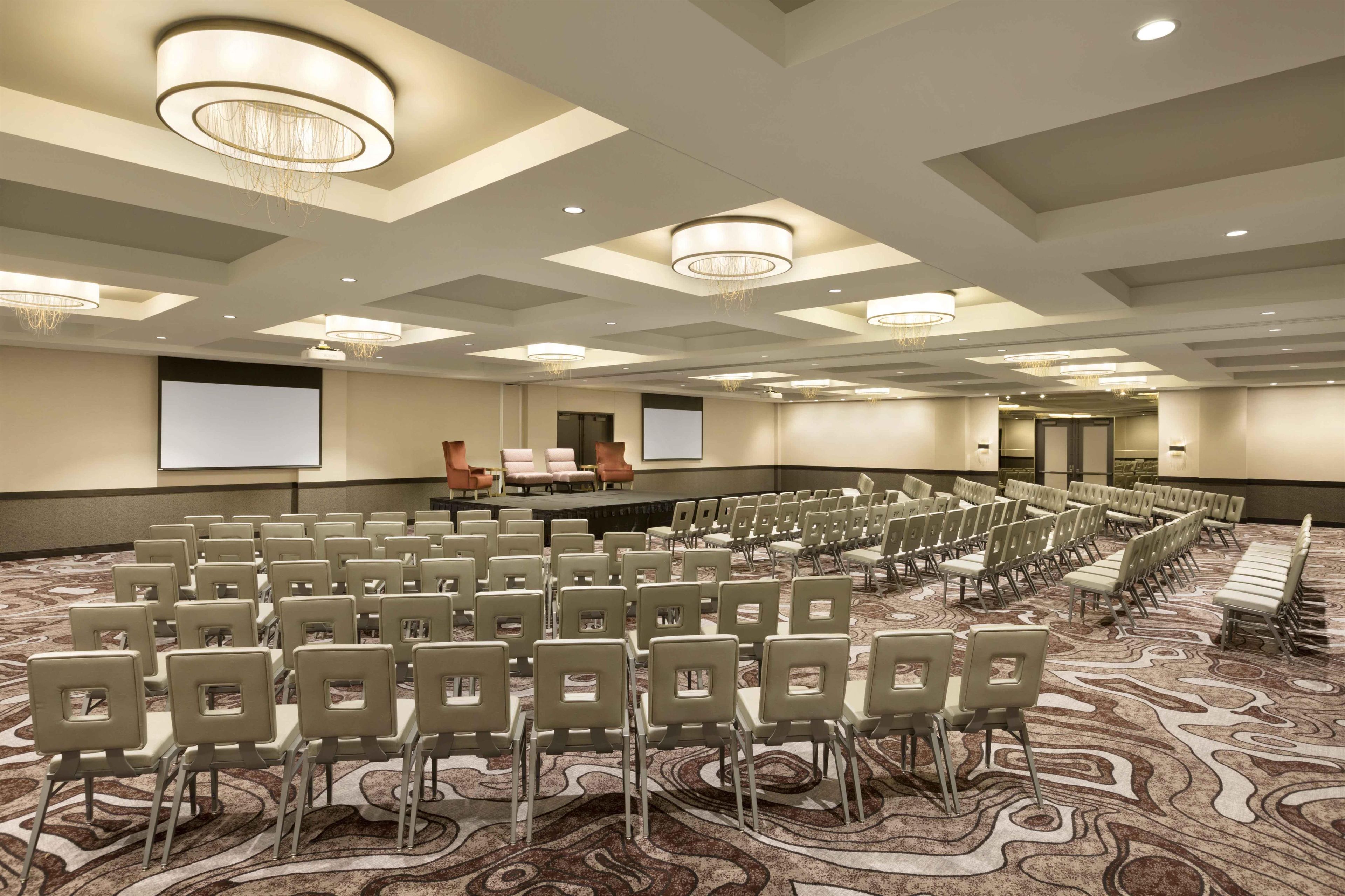 A conference room with rows of chairs, a stage, and a projector screen.