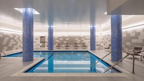 Una piscina con columnas de mosaico azul, sillones de descanso y una pared de azulejos.