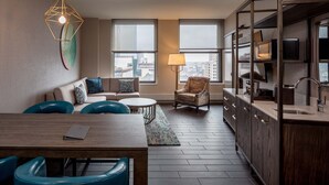 Una sala de estar moderna con sofá, sillas, mesa de comedor y una zona de cocina con lavaplatos y armarios.