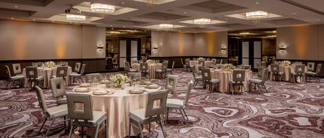 A spacious banquet hall with multiple round tables, each set with chairs and tableware, and a patterned carpet.