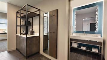 A modern bathroom with a wooden vanity, a large mirror with LED lights, and a built-in shelf with towels.