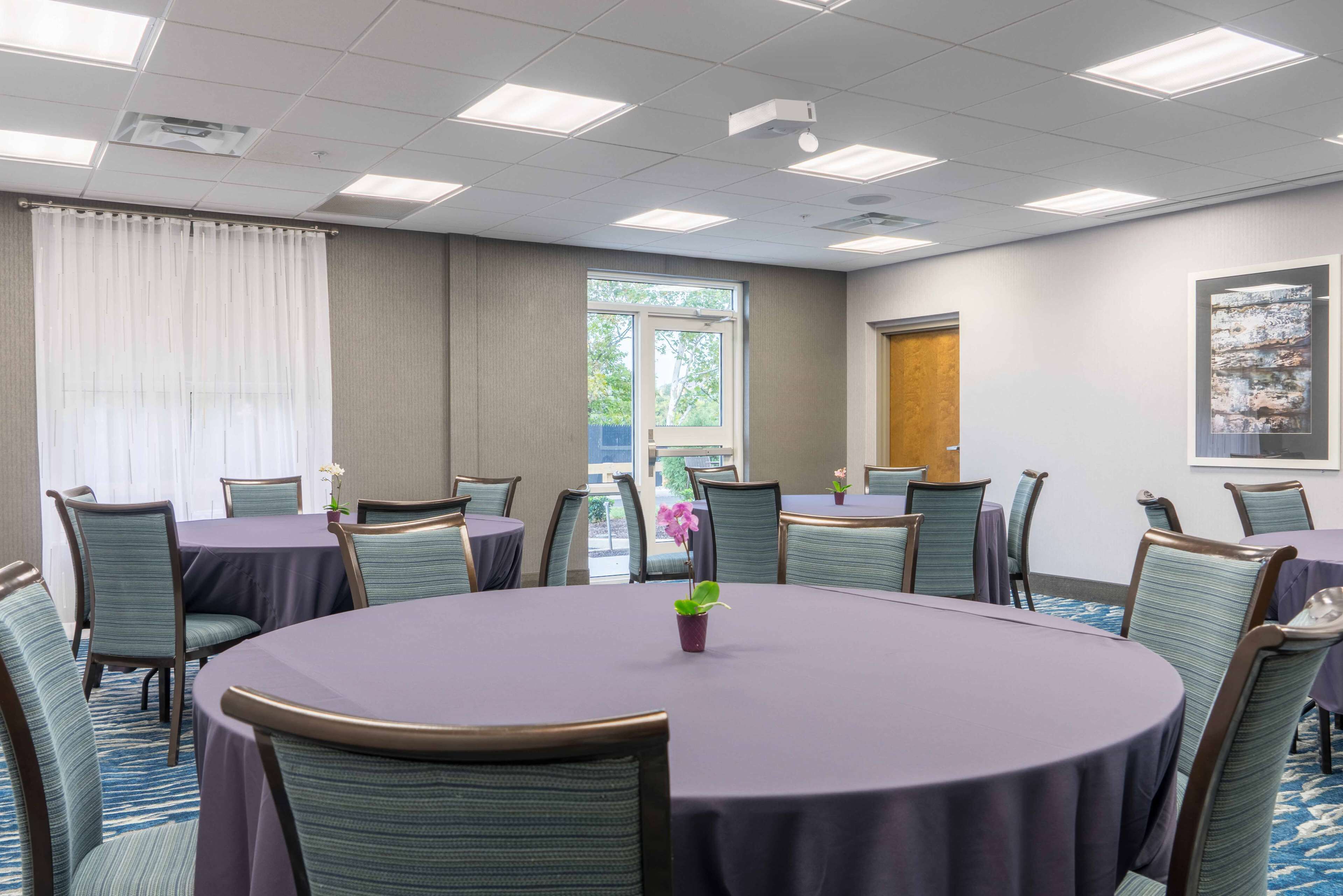 Un salón de conferencias con mesas redondas, sillas y un amplio ventanal con cortinas.