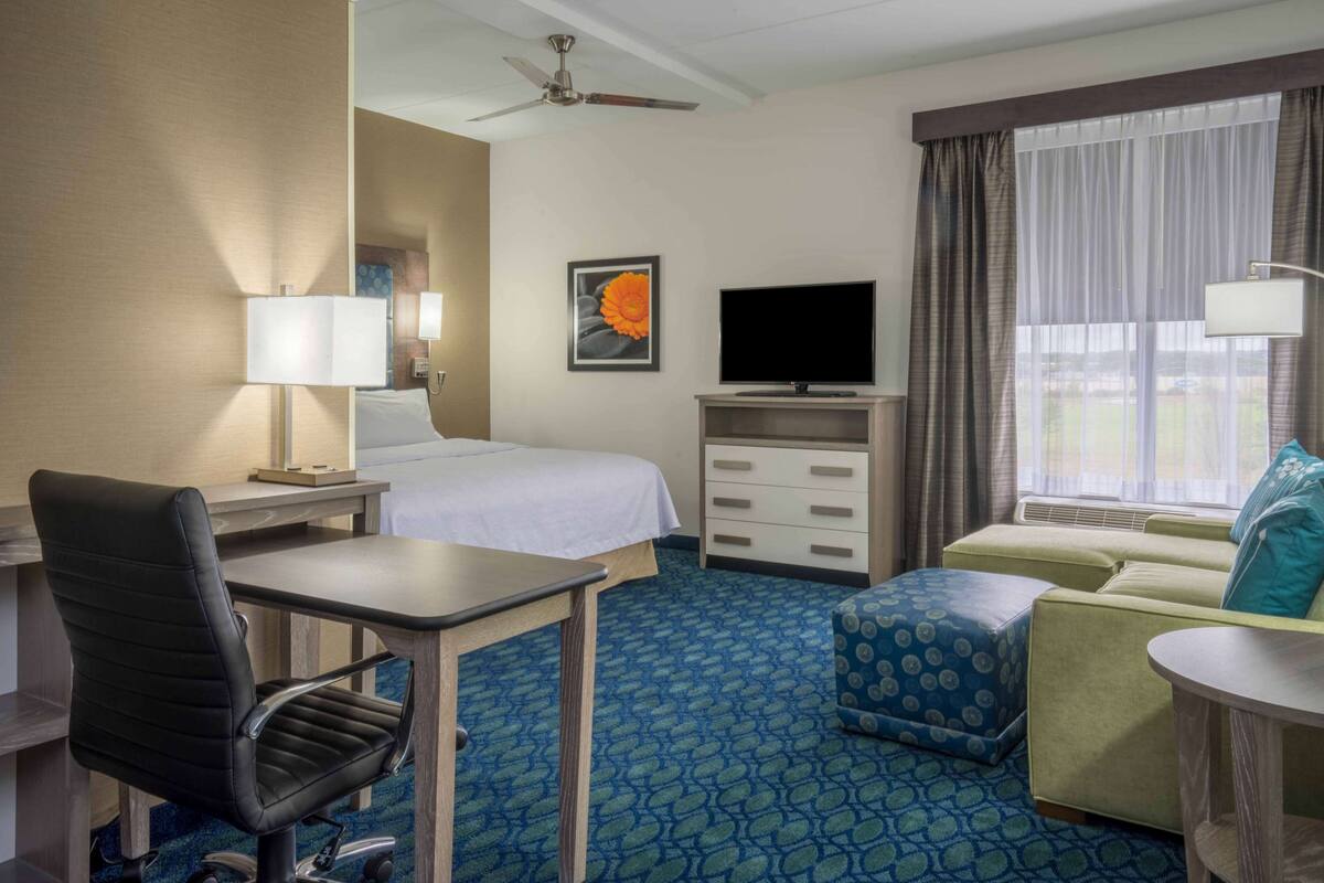 A hotel room with a bed, desk, chair, TV, and a window with curtains.