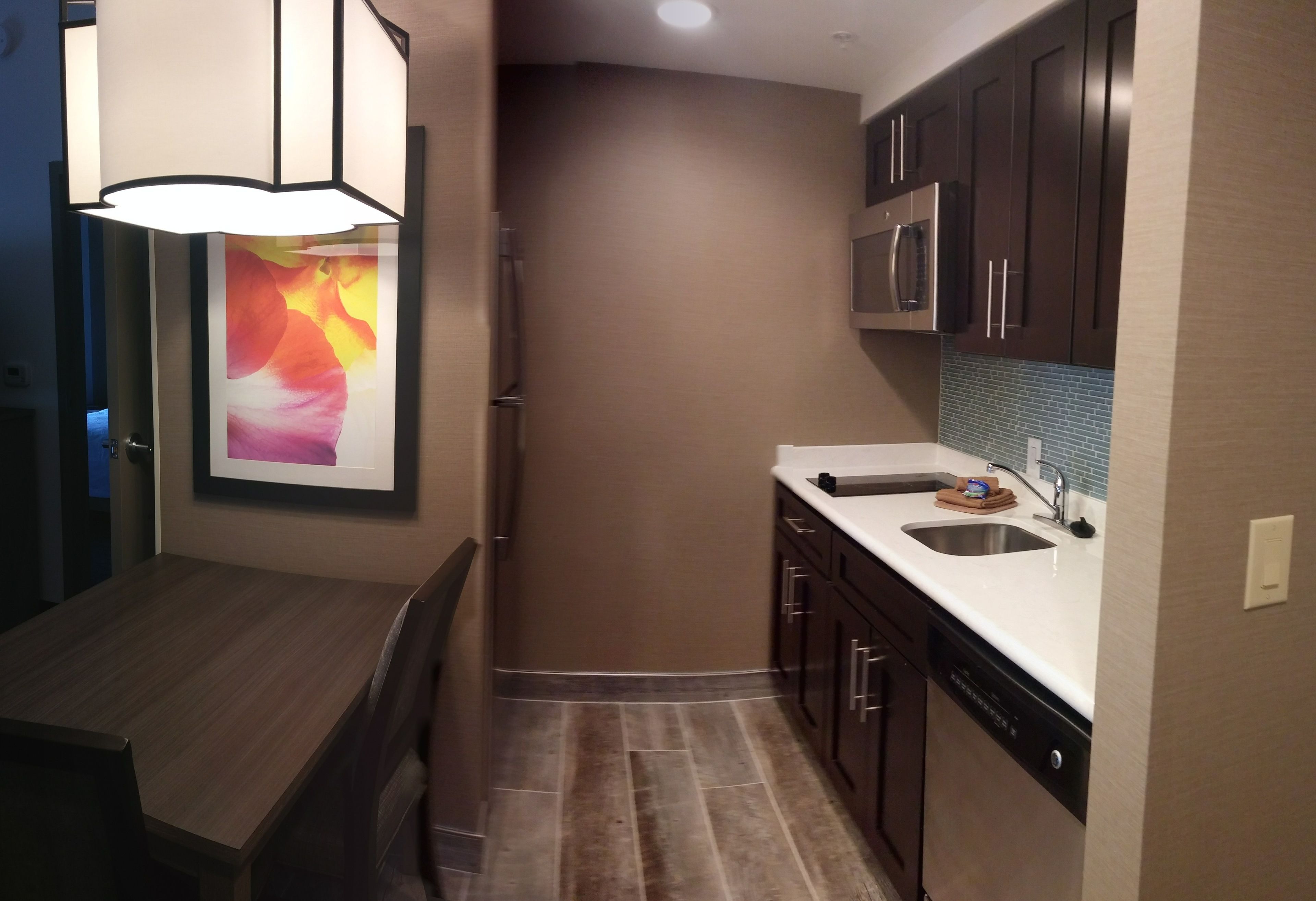 A compact kitchen with dark wooden cabinets, a stainless steel refrigerator, a microwave, and a dishwasher.