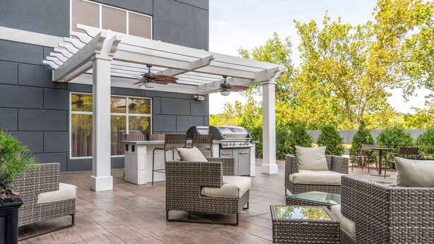 Un patio exterior con mobiliario de mimbre, una pérgola y una zona de barbacoa.