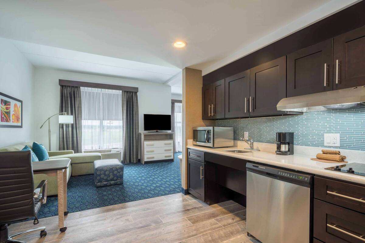 A compact hotel room with a kitchenette, a sofa, a TV, and a dining area.
