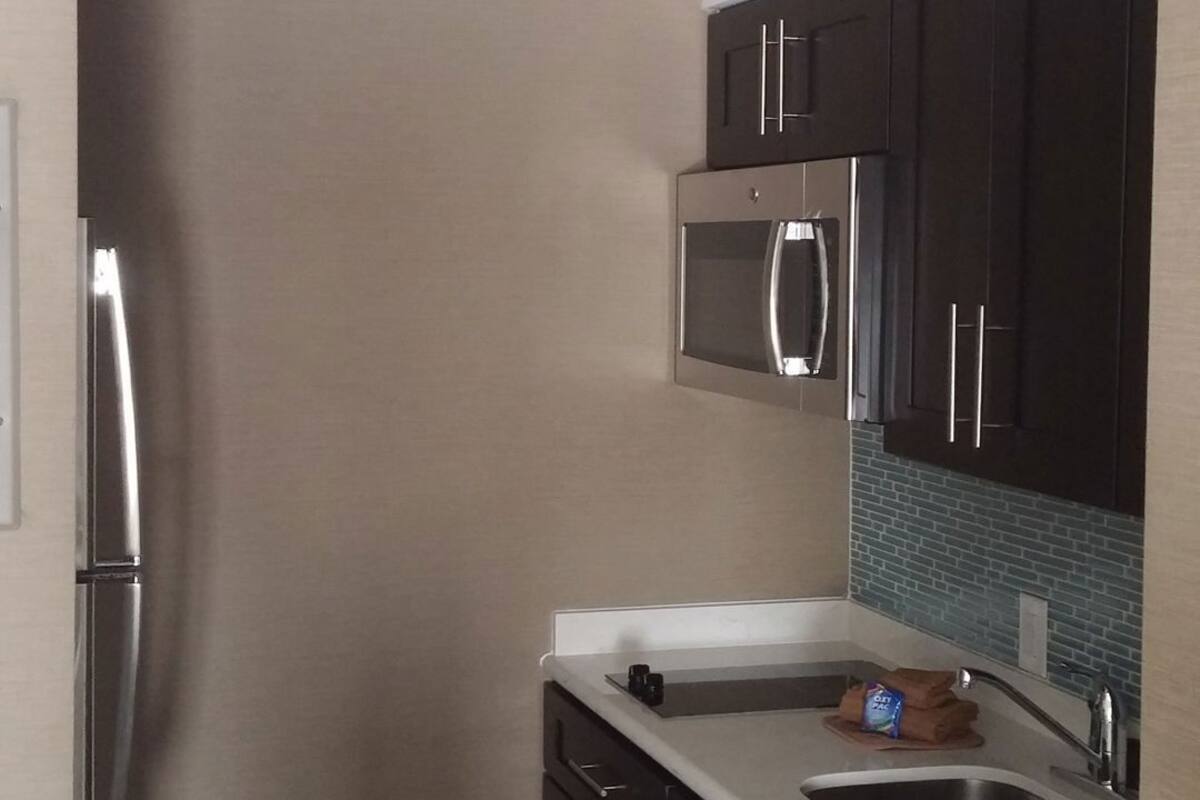 A modern kitchen with dark cabinets, stainless steel appliances, a microwave, and a sink.
