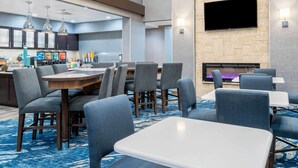 Un hall de hotel con área de bar, zonas de estar y un televisor de pantalla plana en la pared.