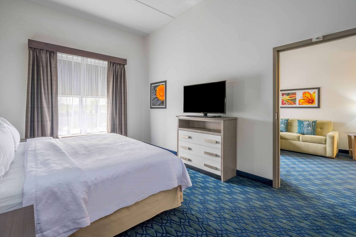 A hotel room with a bed, a television on a stand, a sofa, and a carpeted floor.