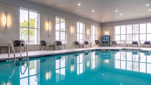 Una piscina interior con agua cristalina, rodeada de ventanas y sillas.