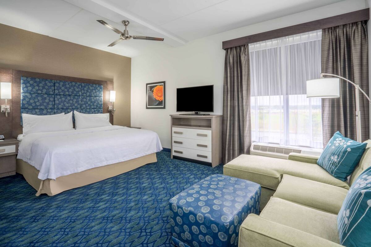 A hotel room with a bed, a TV, a desk, a sofa, and a window with curtains.